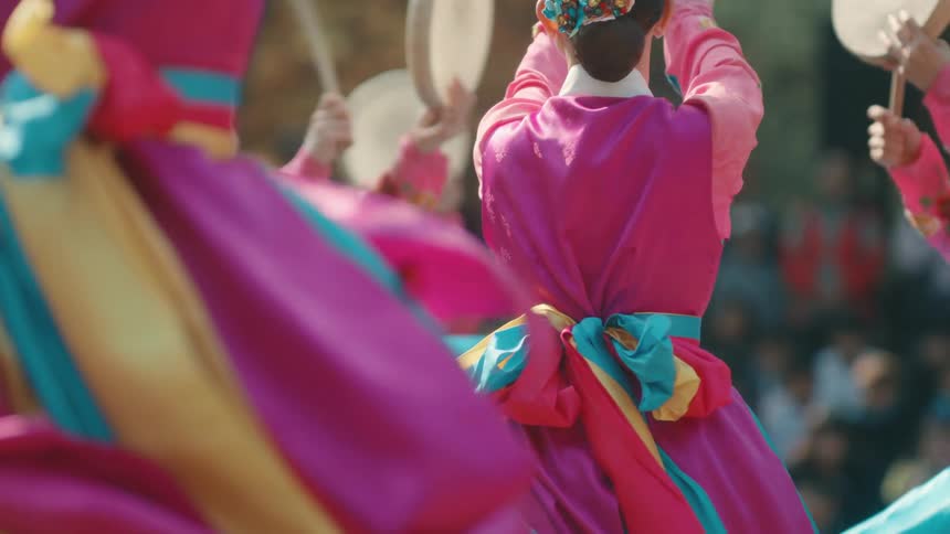 Dances in colorful dresses spin and beat on handheld drums in a park