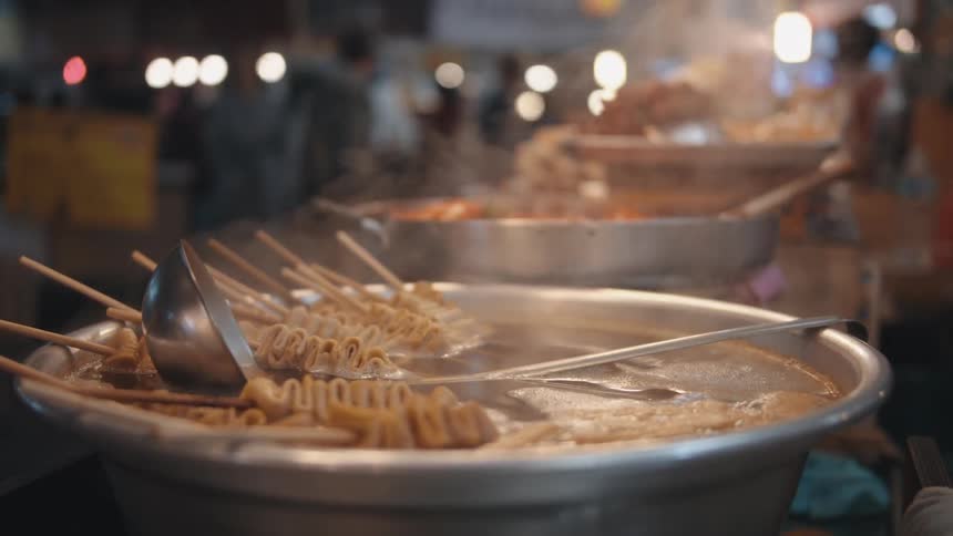 Skewered food sits in a large metal bowl at a night market