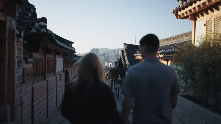 A man and woman hold hands while walking on a city sidewalk