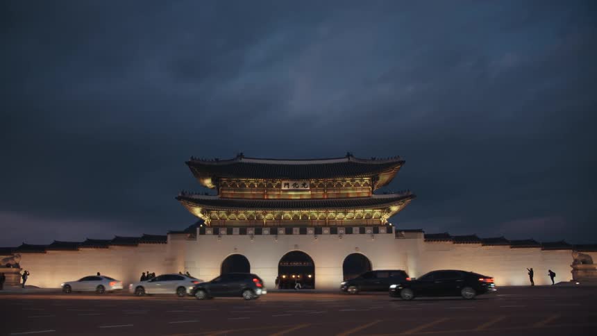 A number of cars drive past an building with distinctive asian architecture