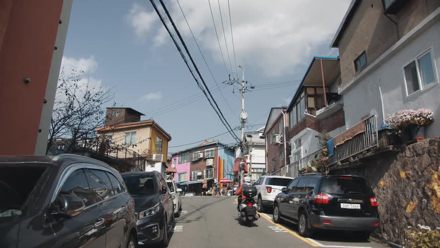 A skinny street with colorful houses and a person driving a motorcycle