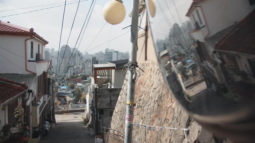 A traffic mirror reflects the buildings around it on a narrow road in a neighborhood