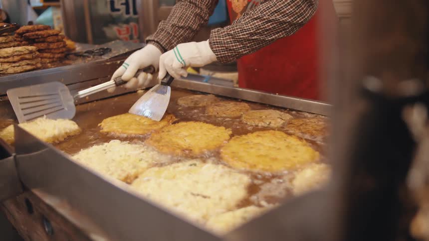 A cook is frying very large potato pancakes in a large vat of oil