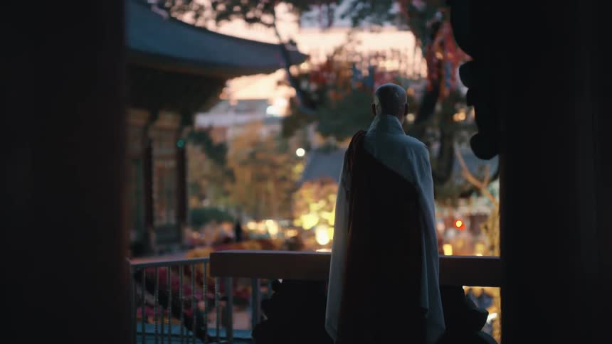 Monk stands on porch overlooking garden at monastery