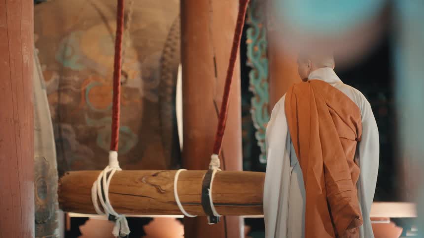 A male monk pushes a large log against something as a gong