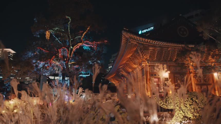 A building with traditional asian architecture is illuminated at nighttime and surrounded by well maintained gardens