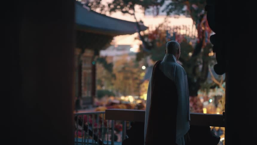 A monk standing a balcony while looking out over the courtyard of a temple