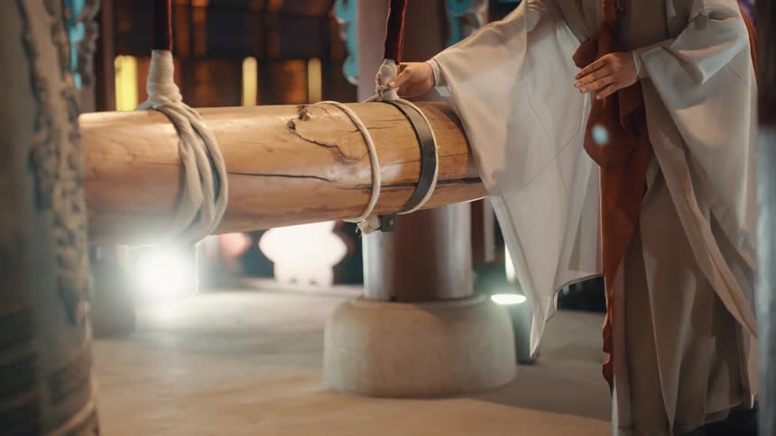 A robed monk uses a large piece of wood to ring a bell