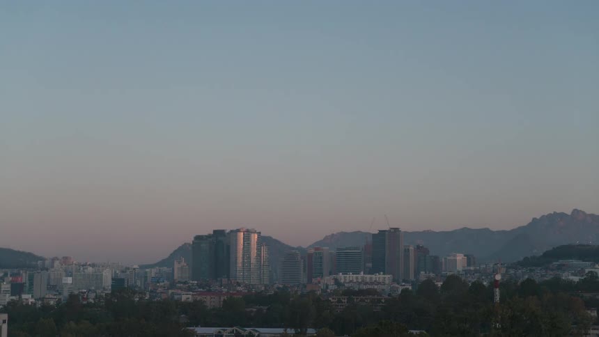 Fog covers city and surrounding forest and mountains as sun rises