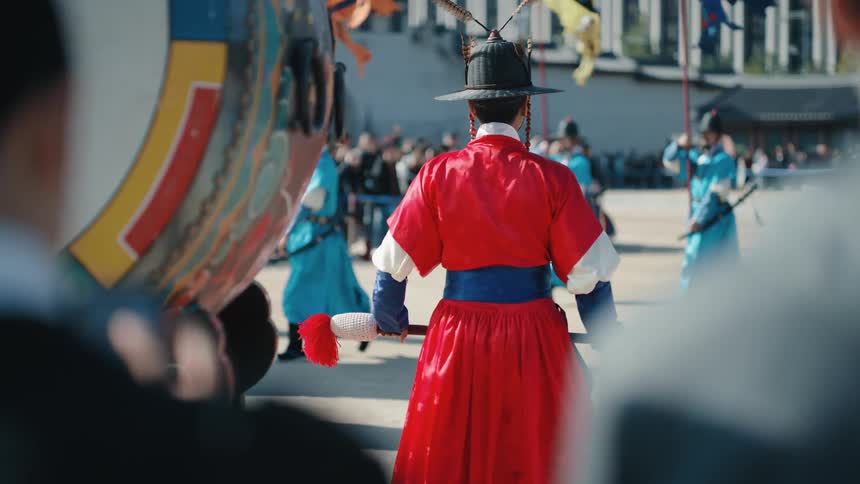 Men in period costume carrying banners march past drummer and audience