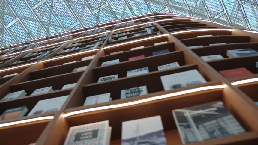 With a building with modern architecture a towering bookshelf is lined with numerous textbooks