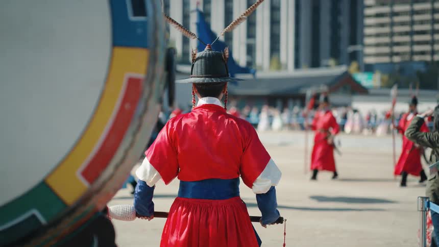 A costumed figure watches a procession nearby