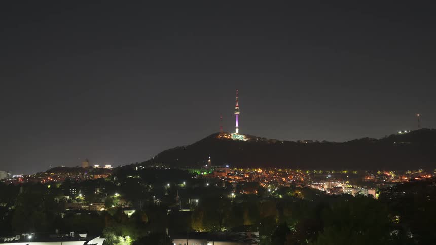 A city neighborhood at the bottom of a hill is lit up at night
