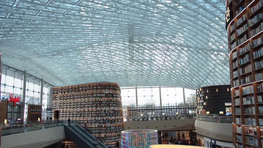 The top level of a busy bookstore is filled with shelves of books with an escalator connecting to the first floor