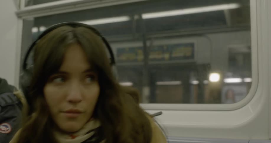 Woman wearing headphones putting her phone away and standing up in a subway