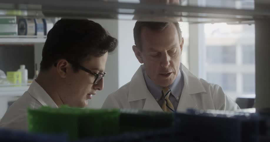 Two people in lab coats talk while looking at something