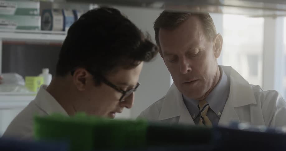 Two scientists in white laboratory coats stands together and discuss results in a laboratory
