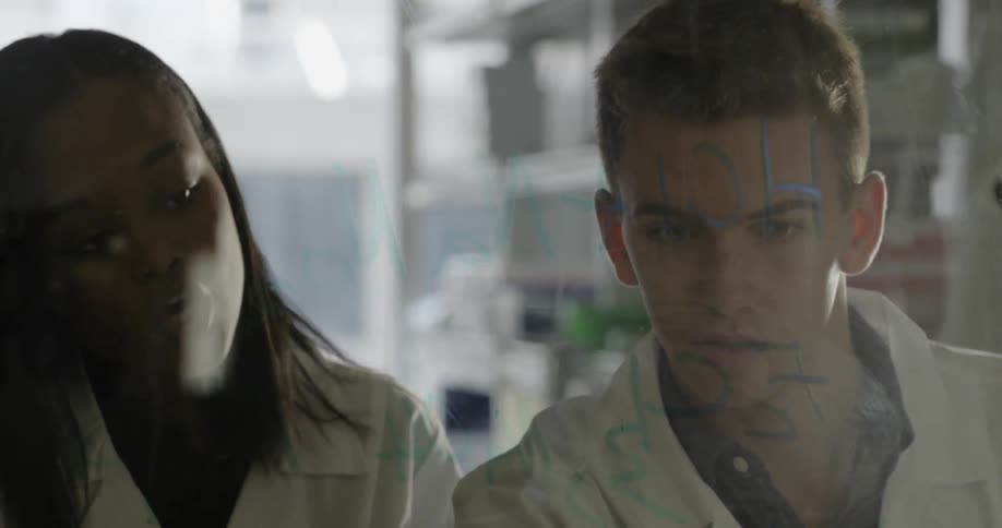 A woman helps a colleague with an equation on a white board