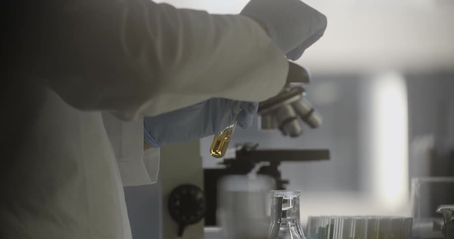 A scientists gloved hands fill a test tube with yellow liquid from another tube