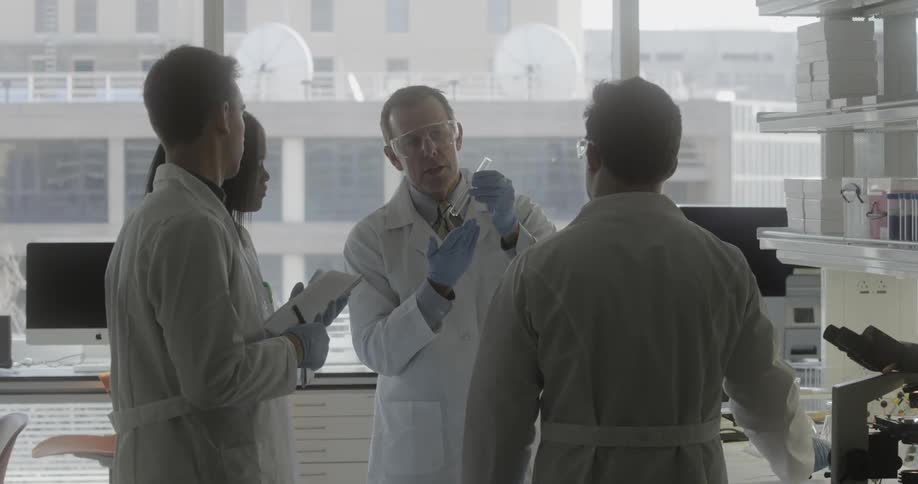 A group of people in lab coats look at a test tube