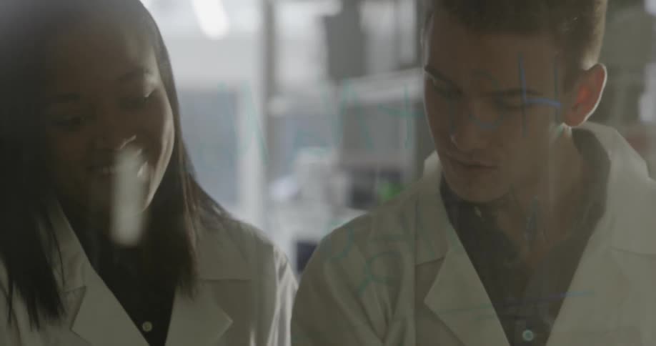 A man and woman wearing lab coats talk and smile as they work on a problem side by side
