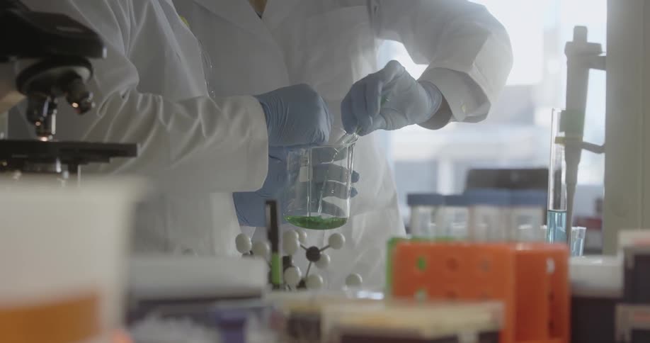 Lab techs mix liquids in a glass container