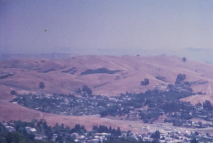 Old footage of a wide shot of hazy mountains and the ocean on a breezy day