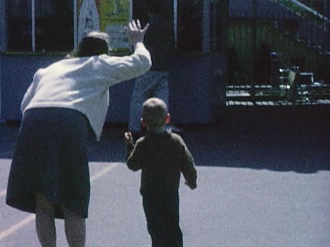 Old footage of a woman and a small boy standing together when the woman waves at someone