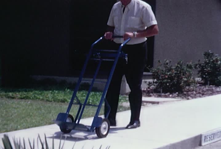 A man pushes an empty hand cart down the sidewalk