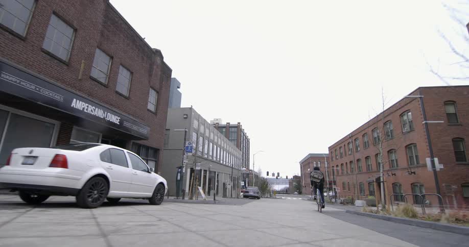 A man is riding a bike down a city street on a cloudy day