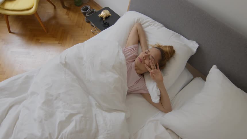 Woman lying in bed stretches and sits up