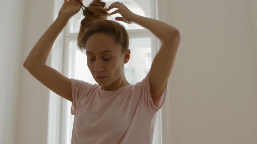 Woman walks through room past windows as she takes down her hair