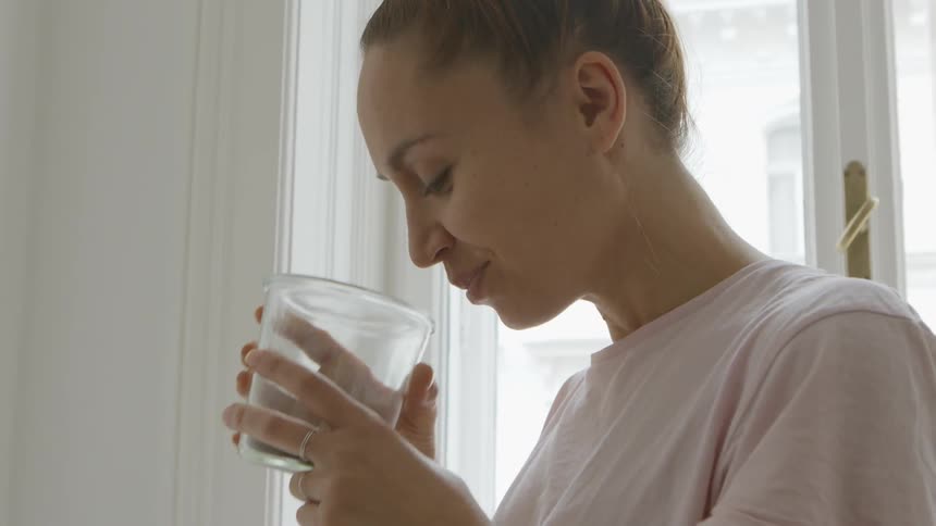 A woman smells a drink in her room
