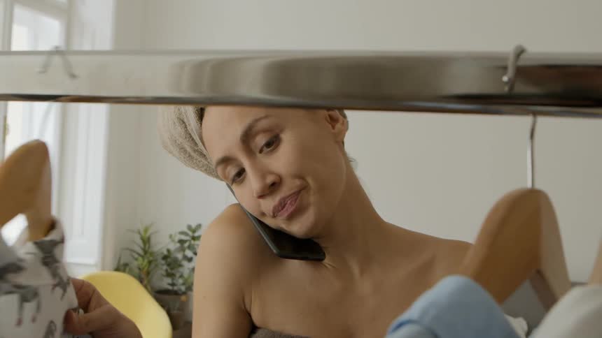 A woman looks at clothes on hangers while talking on a cell phone