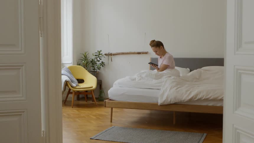 A woman sits up in bed and looks at her phone