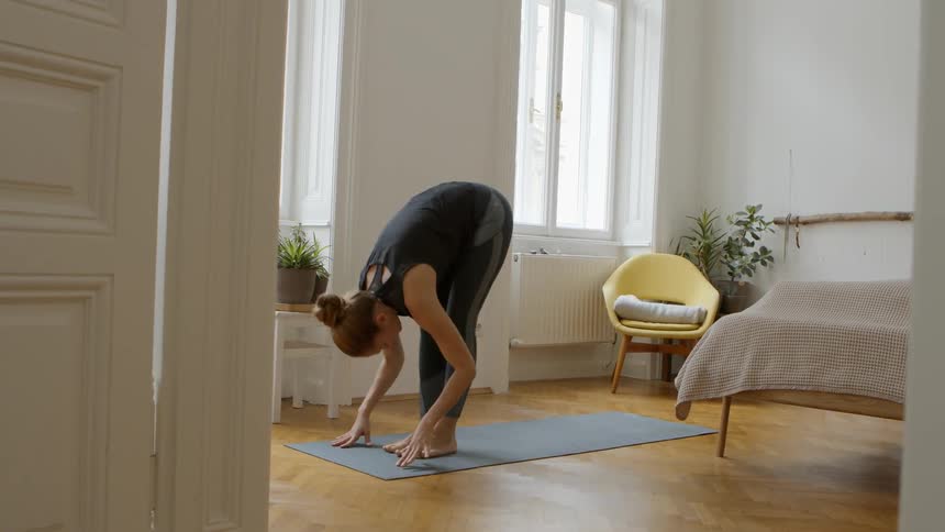 Woman performs yoga poses on yoga mat in bedroom
