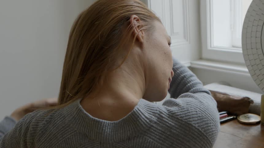 A woman sits in front of a mirror and combs her hair