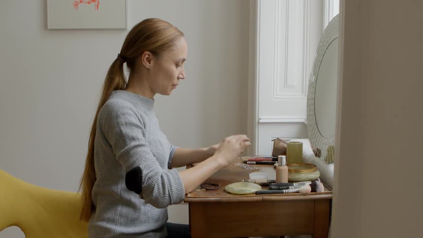 A woman sitting in front of a mirror putting cream on her face