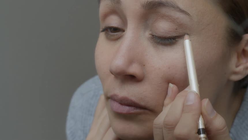A woman applies eyeliner