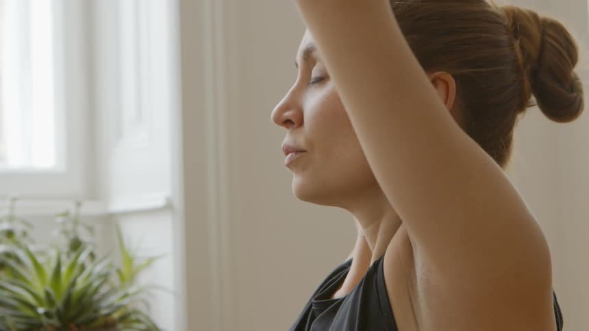 Woman stretches and poses near window and potted plant