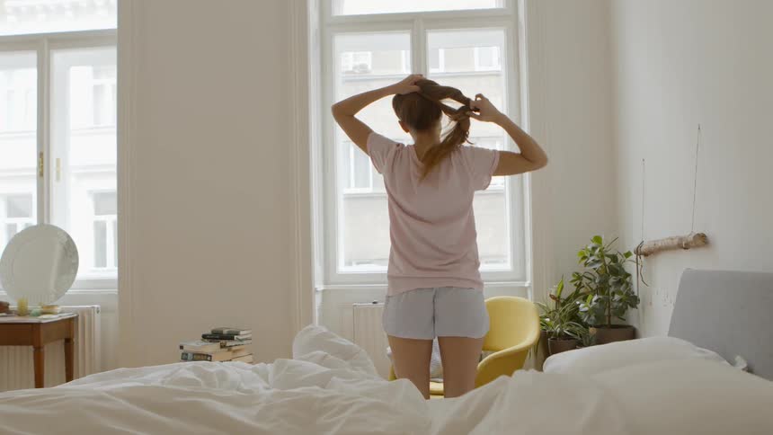 A woman just woke up and is stretching near her bed