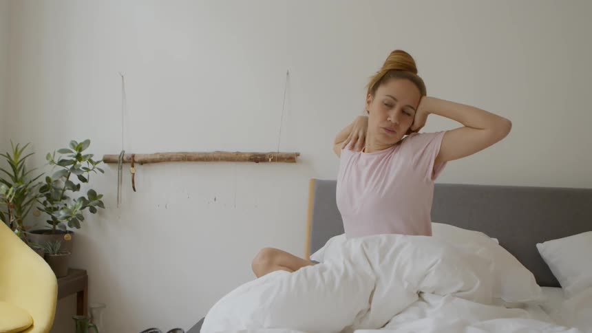 Woman sits in bed stretching