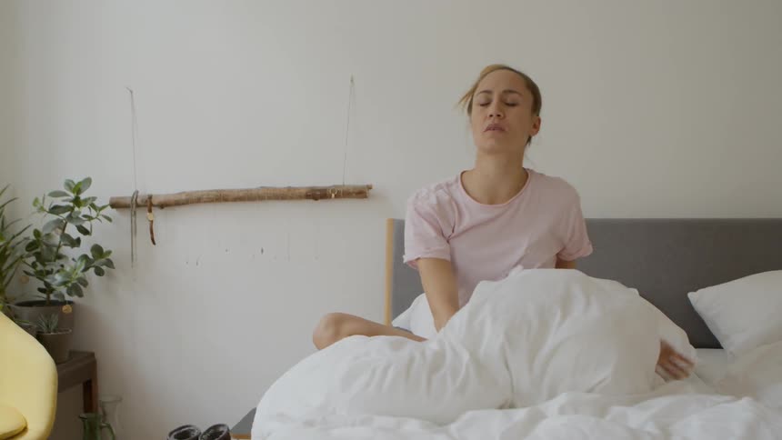 A woman rubs her eye after waking up in bed