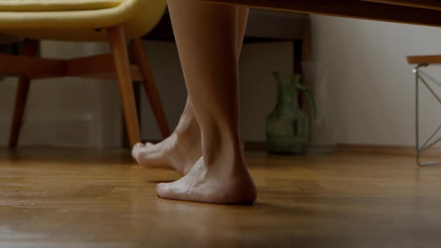 A person lowers their feet to the ground and begins walking on a wooden floor