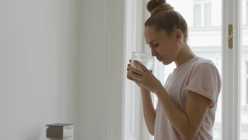 Woman smells freshly made coffee on apartment kitchen at day