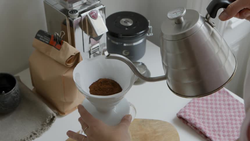 A person pours hot water from a tea kettle in to a cup with grounds in it