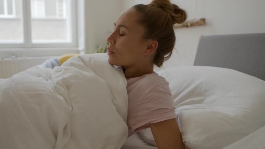 Woman wakes up rubs eyes and sits up in bed