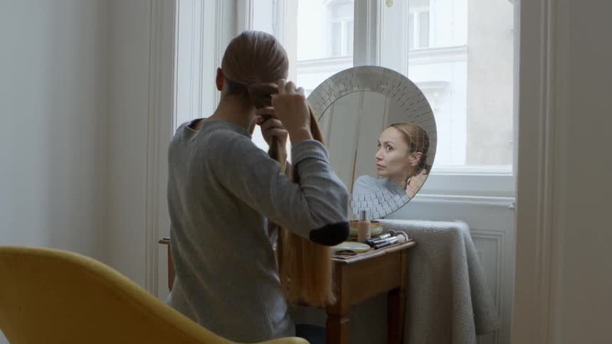 A woman braids her hair in front of a mirror
