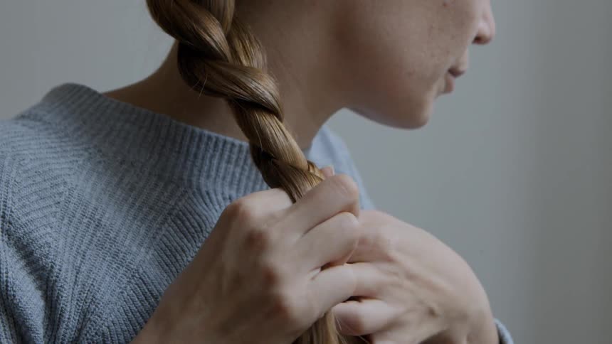 A woman in a sweater braiding her hair