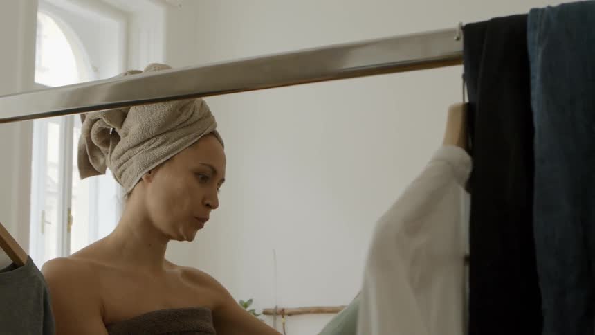 Woman with her hair wrapped in a towel selects clothing from a rack